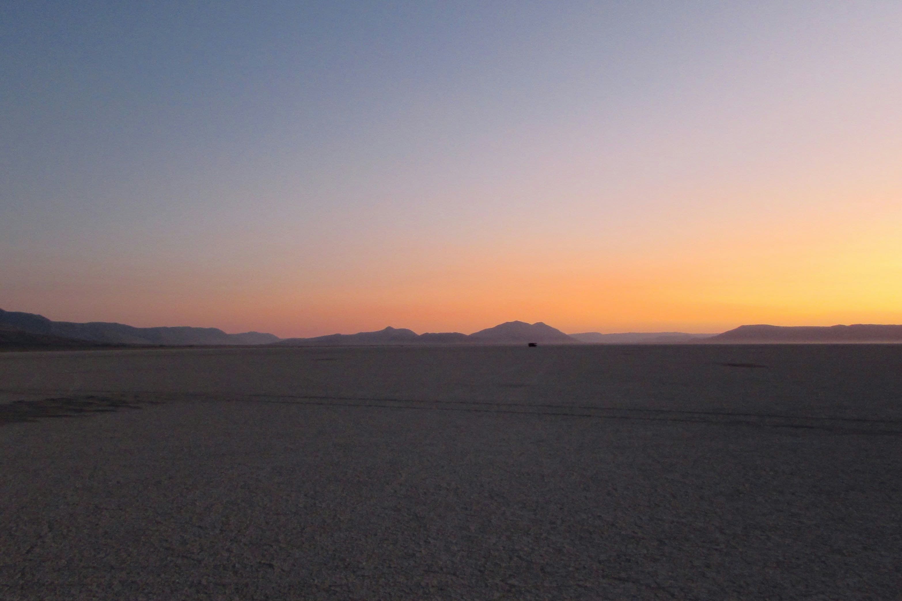 Orange dawn light above distant hills across the Alvord Desert playa