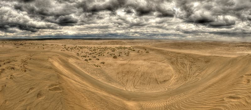 Wind-shaped Christmas Valley sand dunes beneath dark clouds