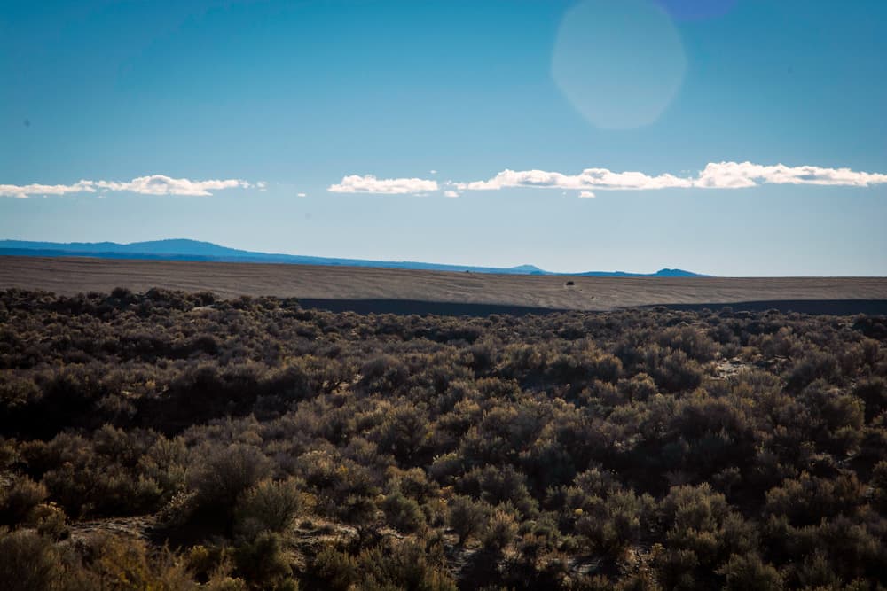 Sagebrush-covered dunes with distant hills beneath scattered clouds